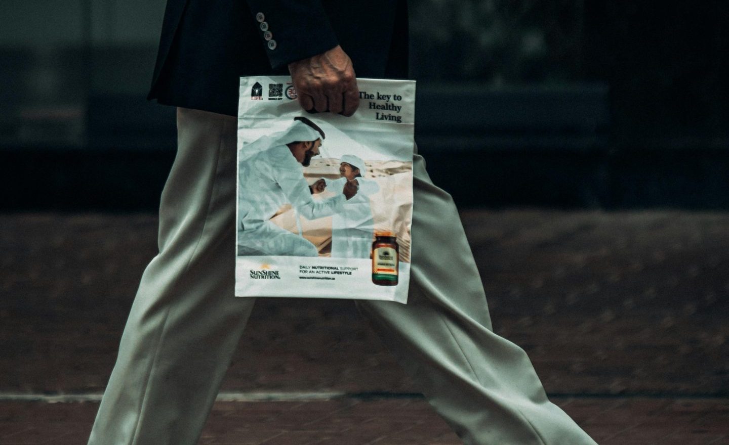 Side view of a businessman in Dubai holding a magazine while walking.